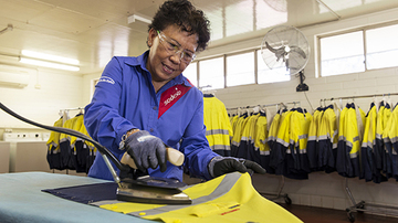Woman ironing bright yellow uniform jackets in the background
