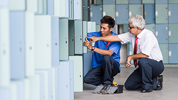Two facilities management employees talking, holding a tablet with screens showing data in the background