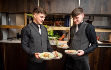 Two men in a restaurant holding plates of food, enjoying a delicious meal together