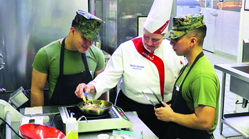A chef teaching two soldiers how to cook